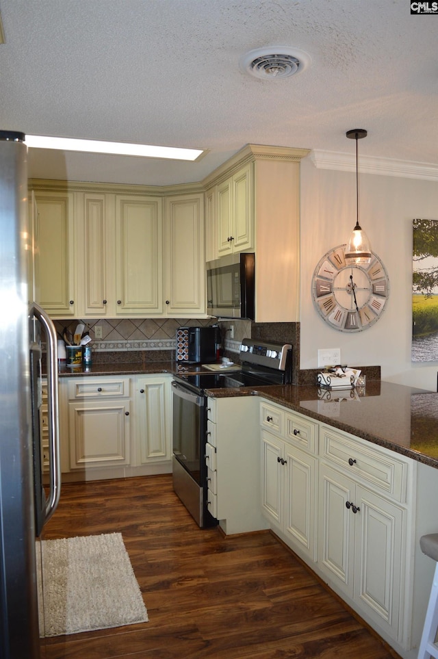 kitchen with cream cabinetry, stainless steel appliances, visible vents, backsplash, and dark wood-type flooring