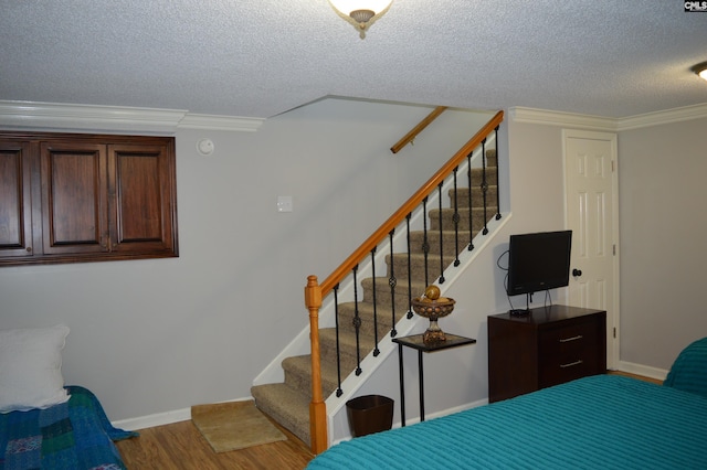 bedroom featuring crown molding, a textured ceiling, baseboards, and wood finished floors