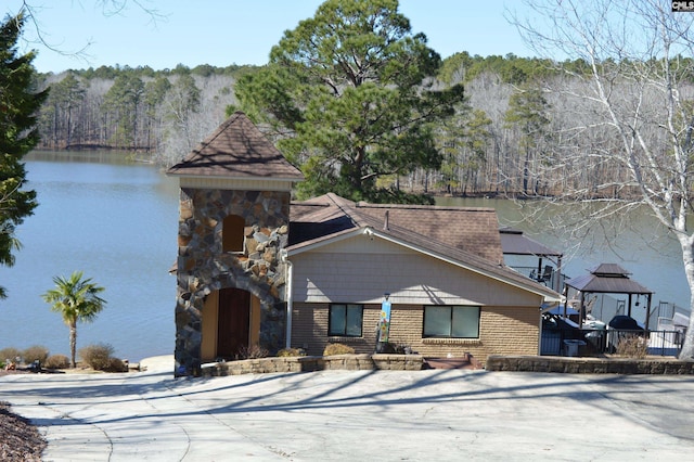 view of front of home featuring brick siding, a wooded view, a gazebo, and a water view