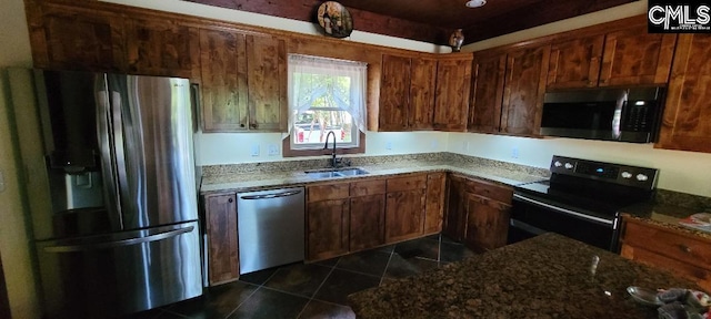 kitchen featuring dark stone counters, stainless steel appliances, dark tile patterned floors, and a sink