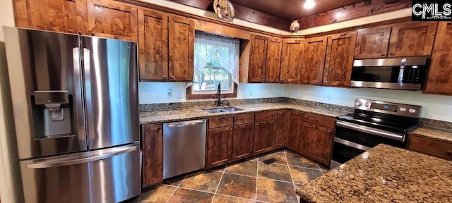 kitchen featuring appliances with stainless steel finishes, brown cabinetry, dark stone countertops, and a sink