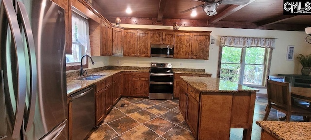 kitchen with beam ceiling, brown cabinets, stainless steel appliances, stone countertops, and a sink