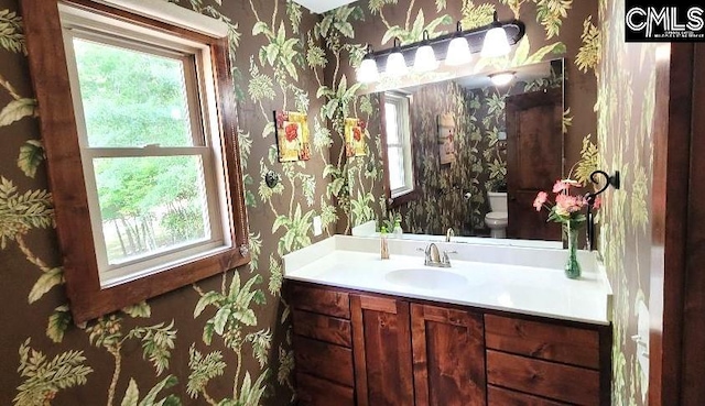 half bathroom with vanity, toilet, and wallpapered walls