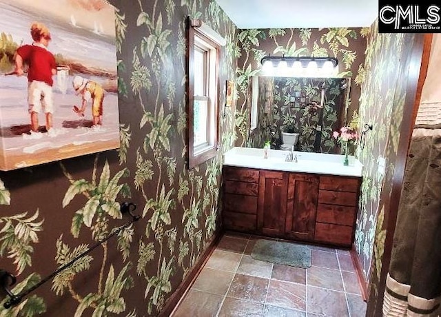 bathroom with baseboards, stone finish flooring, vanity, and wallpapered walls