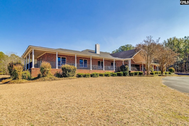 ranch-style home featuring a chimney, a porch, and brick siding