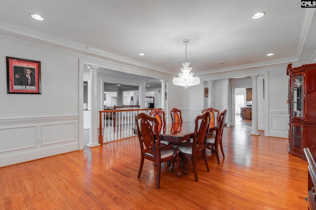 dining room featuring light wood-style floors, a decorative wall, ornate columns, and ornamental molding