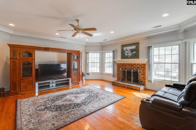 living room featuring ceiling fan, wood finished floors, visible vents, a brick fireplace, and crown molding