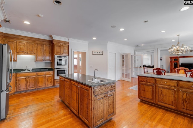 kitchen featuring stainless steel appliances, brown cabinetry, a sink, and an island with sink