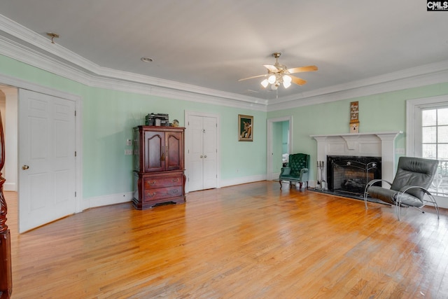 living room with a fireplace with raised hearth, light wood finished floors, baseboards, and crown molding