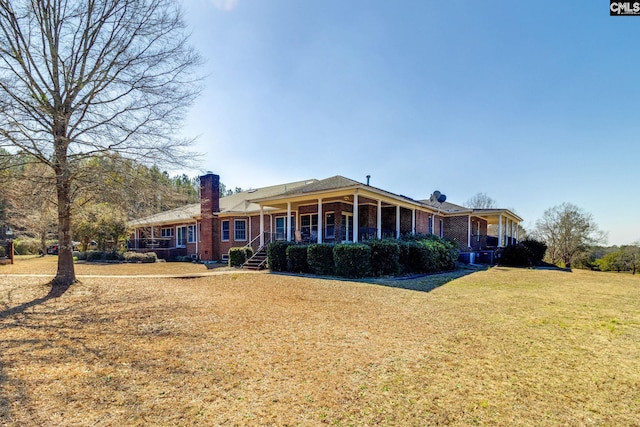 back of property with covered porch, brick siding, a lawn, and a chimney