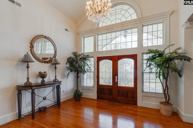 entryway with high vaulted ceiling, wood finished floors, visible vents, and a notable chandelier