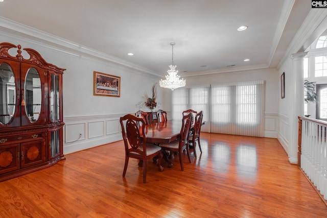 dining space featuring crown molding, a notable chandelier, a decorative wall, and light wood finished floors