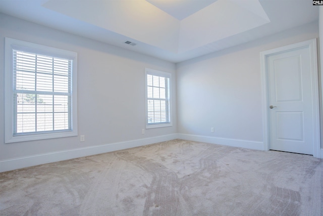 carpeted empty room featuring a raised ceiling, visible vents, and baseboards