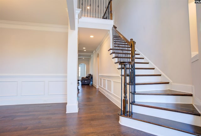 staircase with arched walkways, recessed lighting, a decorative wall, ornamental molding, and wood finished floors