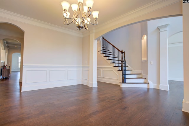 spare room featuring arched walkways, stairway, dark wood-type flooring, crown molding, and a decorative wall