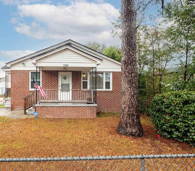 bungalow-style home with a front yard, fence, and brick siding