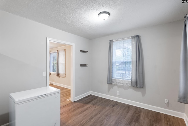 unfurnished room featuring a textured ceiling, baseboards, and wood finished floors