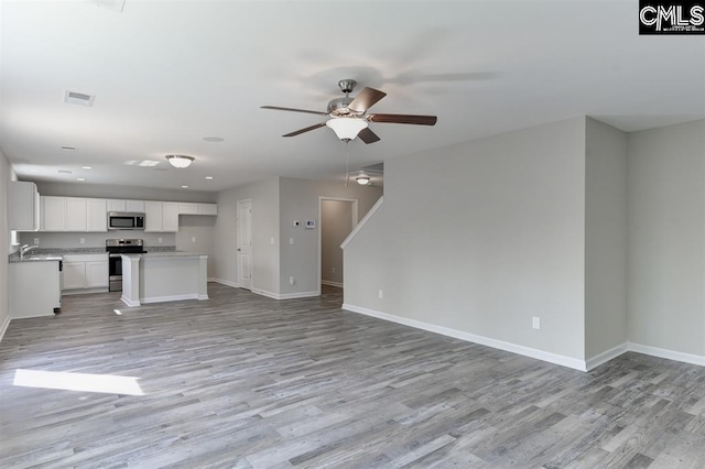 unfurnished living room with light wood-type flooring, baseboards, visible vents, and a ceiling fan