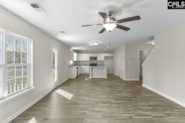 unfurnished living room featuring light wood-style flooring, a ceiling fan, visible vents, and baseboards