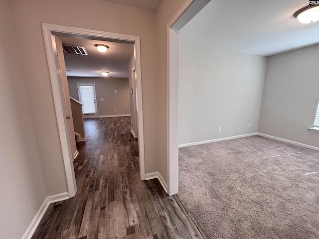 hallway with dark wood finished floors, visible vents, and baseboards