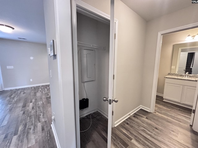 hallway with a sink, dark wood finished floors, electric panel, and baseboards