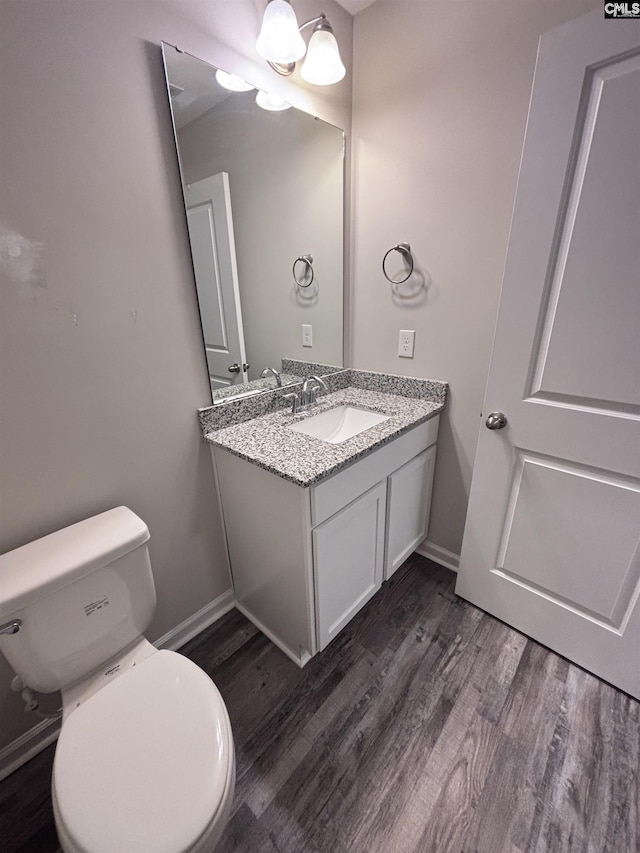 half bathroom featuring toilet, baseboards, wood finished floors, and vanity