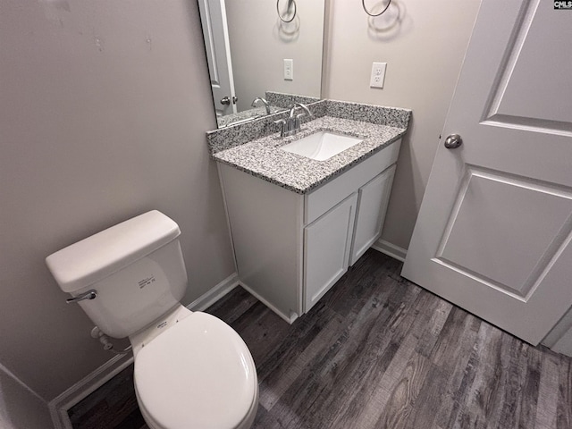 half bathroom with baseboards, vanity, toilet, and wood finished floors