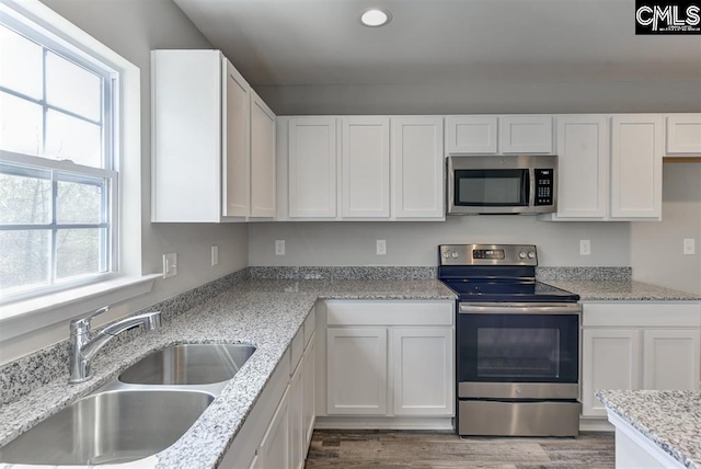 kitchen with light stone counters, stainless steel appliances, white cabinetry, a sink, and light wood-type flooring