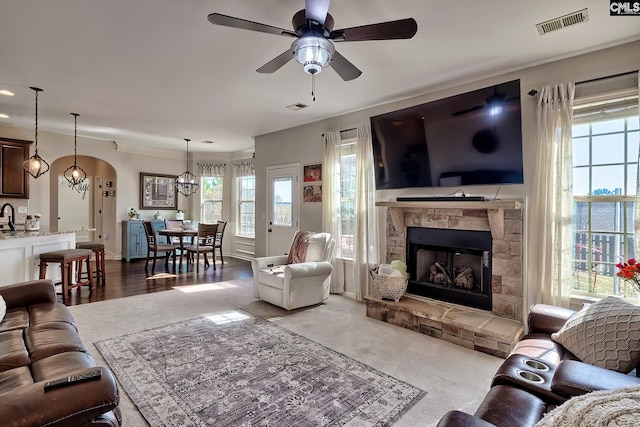 living area with arched walkways, ceiling fan, a fireplace, and visible vents