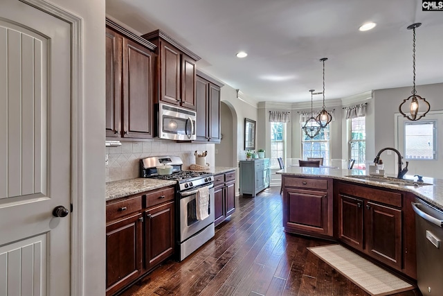 kitchen featuring light stone counters, dark wood finished floors, backsplash, appliances with stainless steel finishes, and a sink