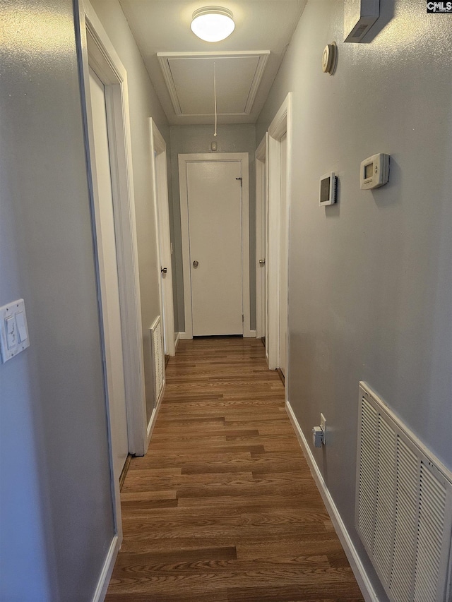 hallway featuring baseboards, wood finished floors, visible vents, and attic access