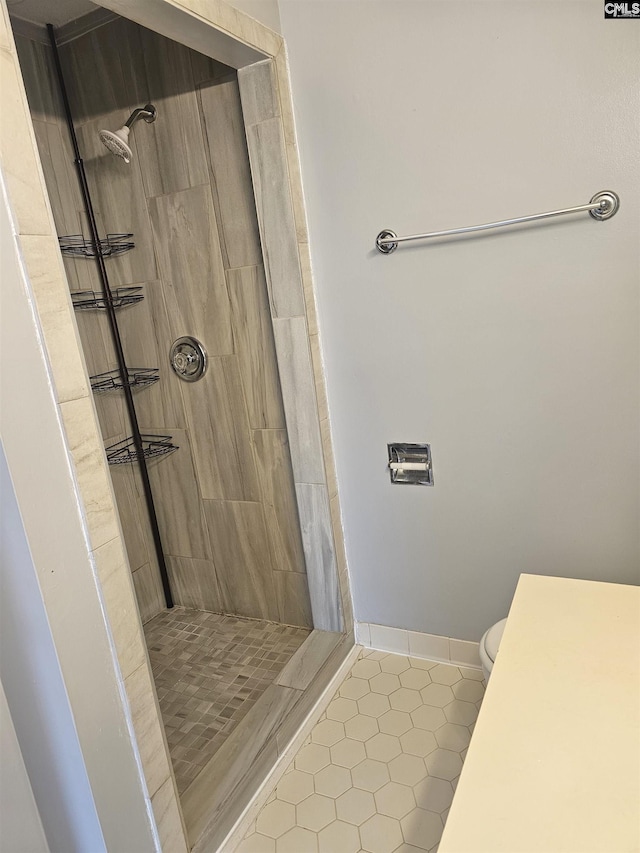 bathroom featuring toilet, a tile shower, baseboards, and tile patterned floors