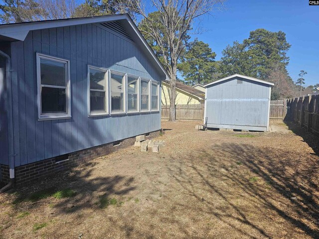 view of property exterior featuring crawl space, a fenced backyard, a storage unit, and an outbuilding