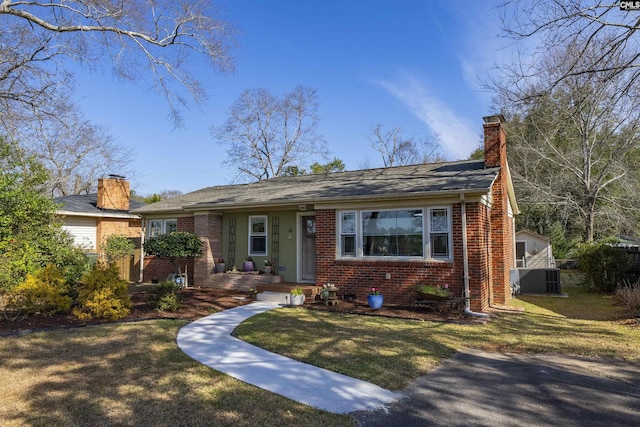 view of front of home featuring brick siding, a chimney, a front lawn, and central air condition unit