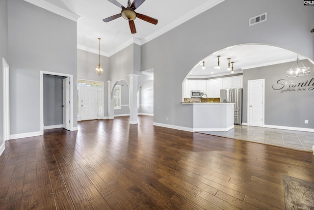 unfurnished living room featuring arched walkways, crown molding, wood-type flooring, visible vents, and baseboards