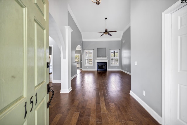 unfurnished living room with a fireplace, dark wood finished floors, a ceiling fan, ornamental molding, and baseboards