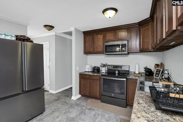 kitchen featuring baseboards, ornamental molding, light stone countertops, stainless steel appliances, and a sink