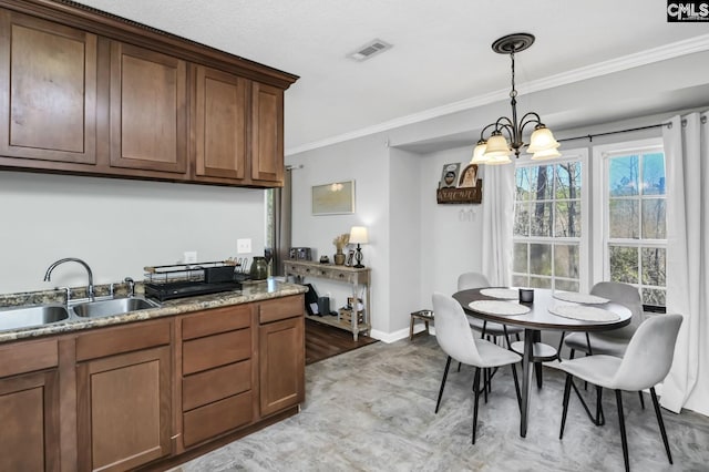 kitchen featuring a sink, visible vents, baseboards, ornamental molding, and pendant lighting