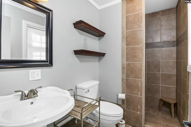 bathroom with a tile shower, ornamental molding, a sink, and toilet