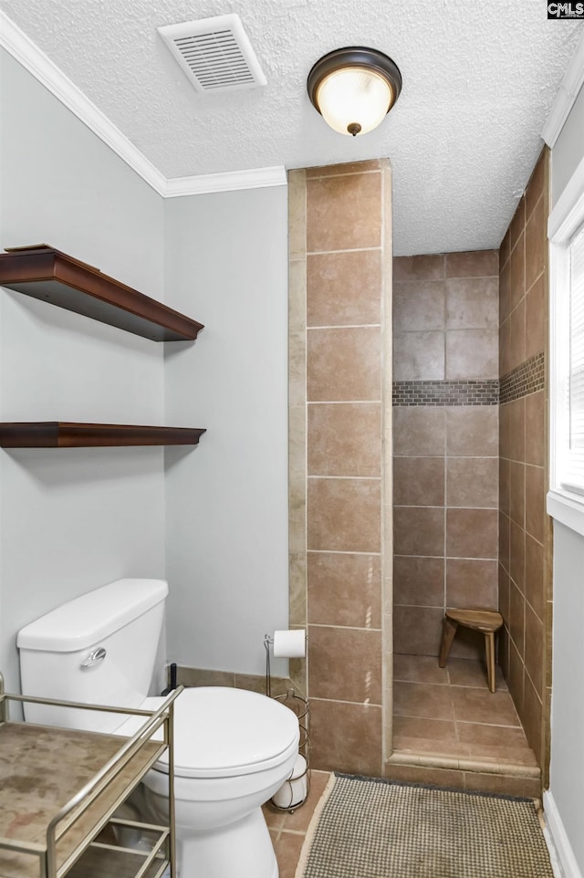 bathroom featuring visible vents, toilet, a tile shower, a textured ceiling, and tile patterned floors