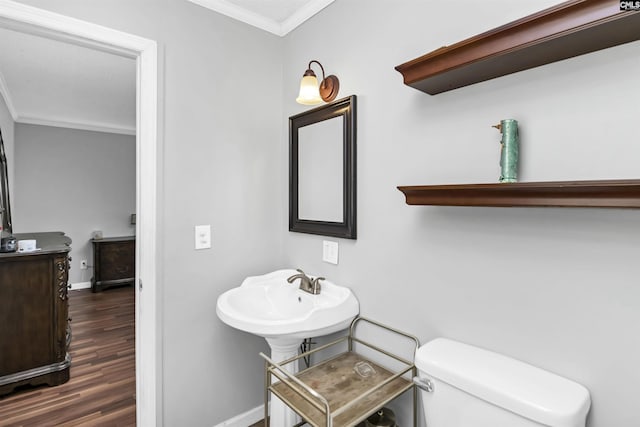 half bath with baseboards, toilet, wood finished floors, crown molding, and a sink