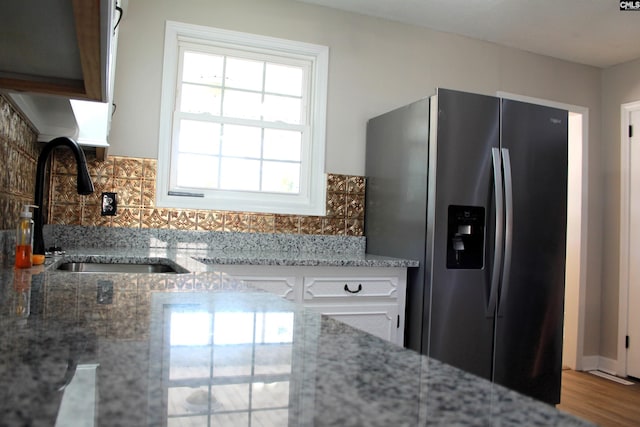 kitchen featuring backsplash, white cabinetry, a sink, light stone countertops, and stainless steel fridge