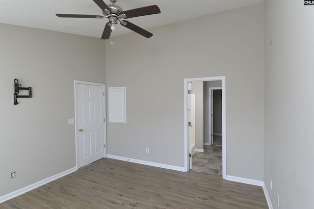 unfurnished room with ceiling fan, a towering ceiling, baseboards, and wood finished floors