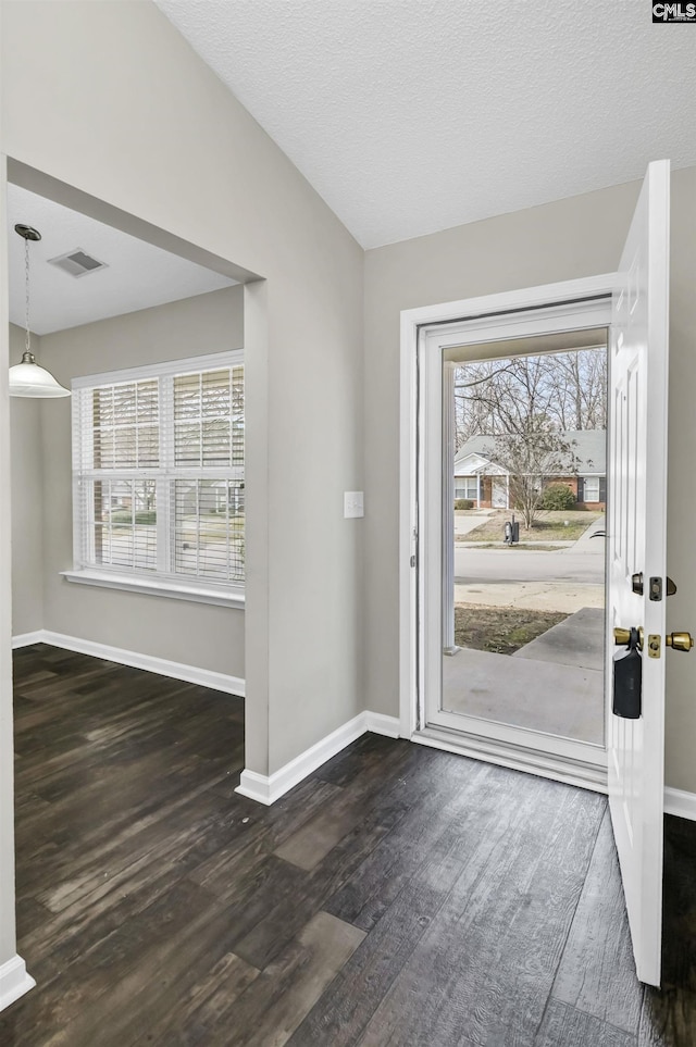 foyer with dark wood-type flooring, lofted ceiling, visible vents, and plenty of natural light