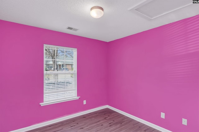 unfurnished room featuring a textured ceiling, wood finished floors, visible vents, baseboards, and attic access