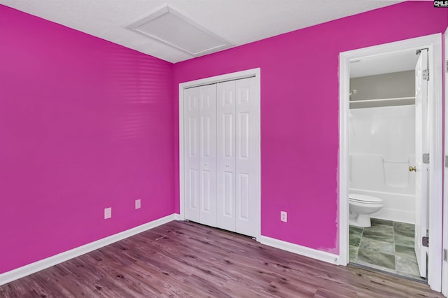 unfurnished bedroom featuring attic access, baseboards, ensuite bath, wood finished floors, and a closet