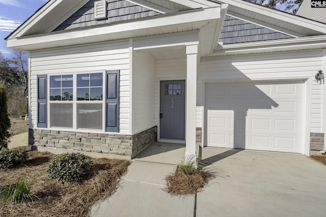 view of exterior entry with a garage, stone siding, and driveway