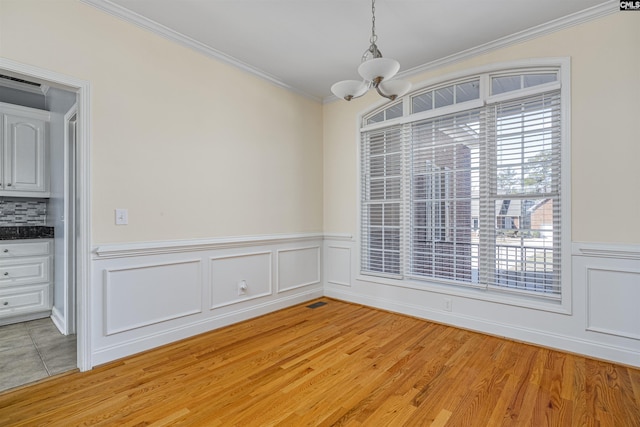 unfurnished dining area featuring light wood-style floors, ornamental molding, a wealth of natural light, and an inviting chandelier