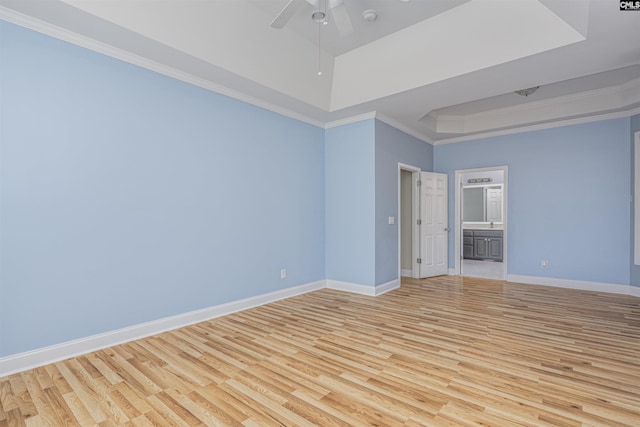 empty room featuring baseboards, a raised ceiling, a ceiling fan, ornamental molding, and light wood-type flooring