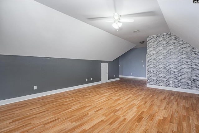 bonus room with a ceiling fan, an accent wall, vaulted ceiling, light wood-type flooring, and baseboards